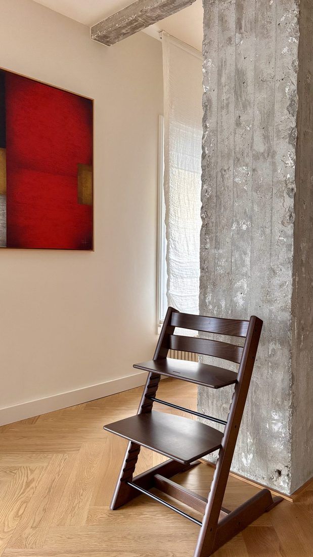 Cuadro rojo y trona de madera junto a un pilar de hormigón en un piso reformado